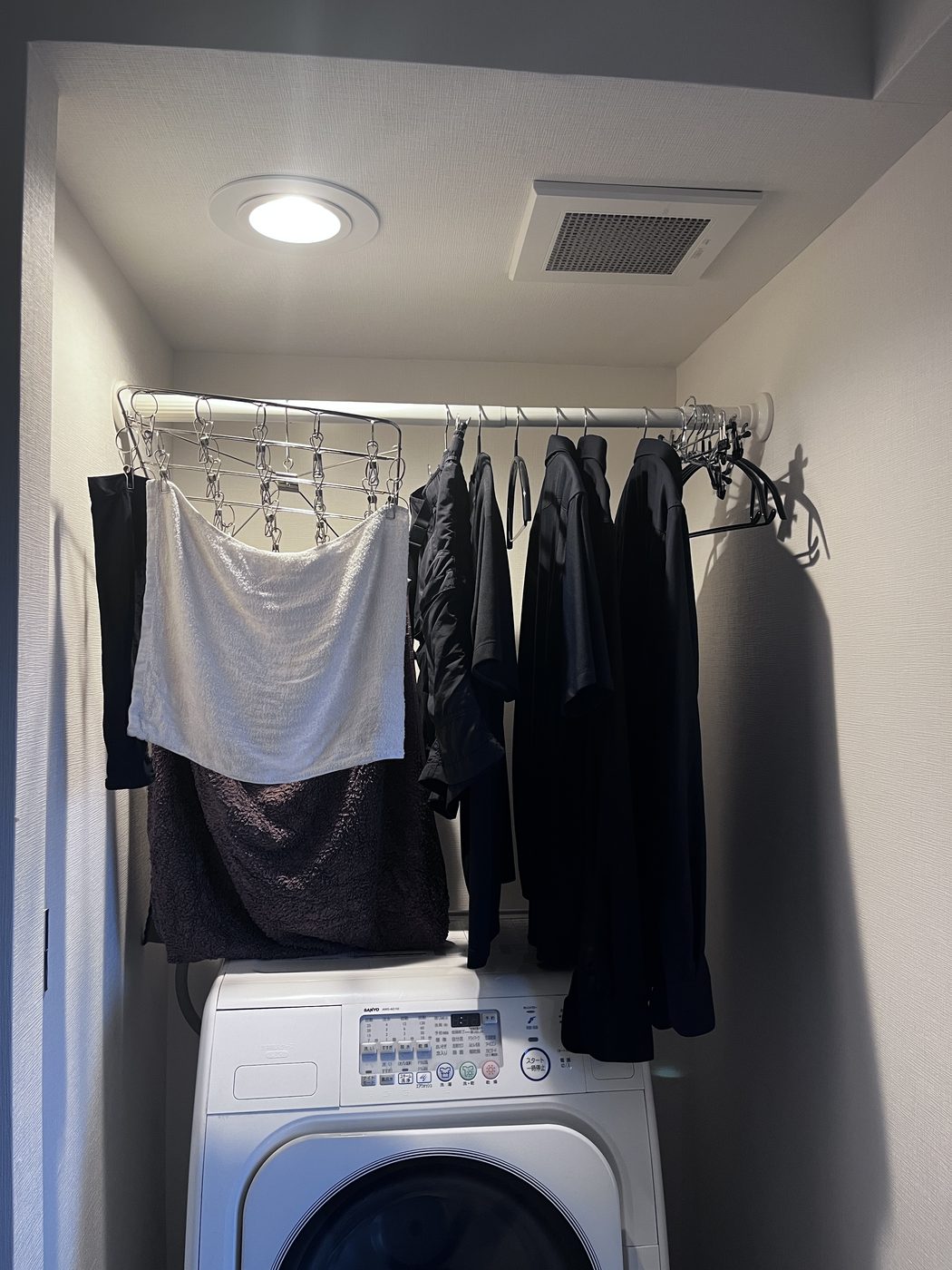 A tension rod spanning the alcove above a washing machine in a Japanese apartment, hung with laundry