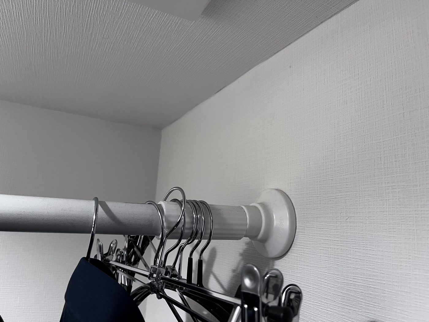 Close-up of the end cap of a tension rod pressed against a wall, holding hangers