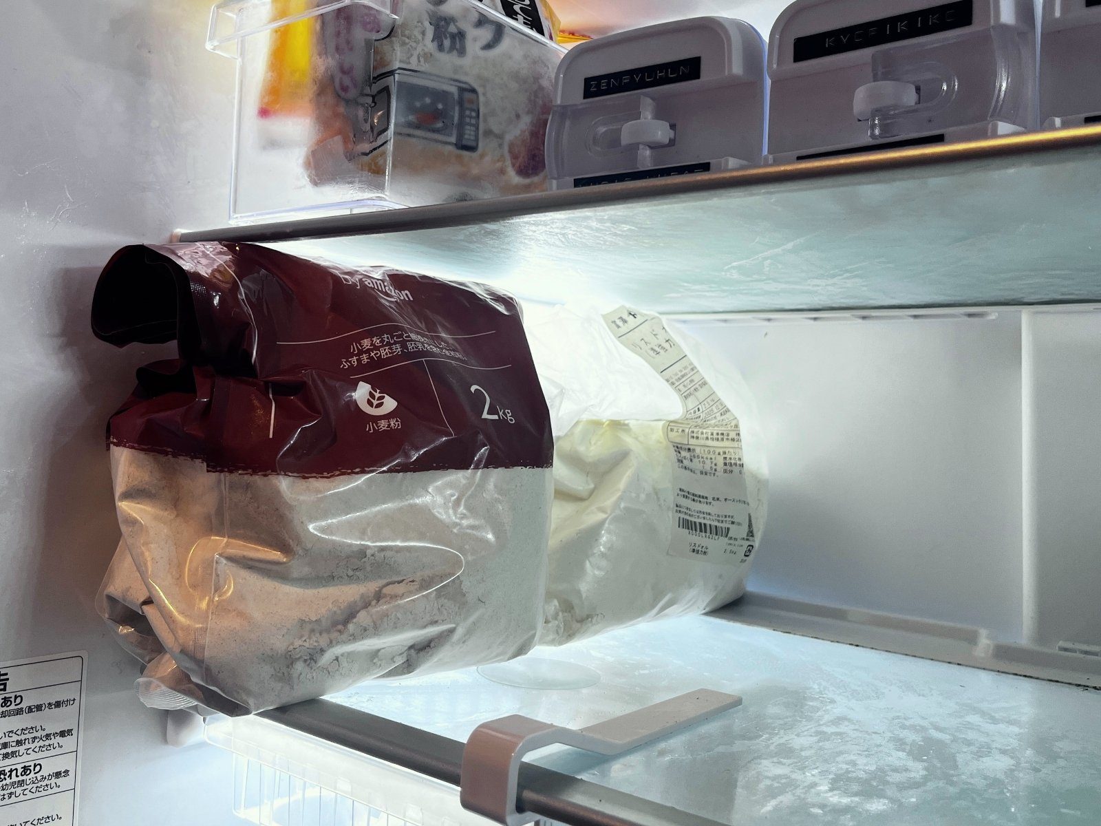 Two large bags of flour lying on a lower fridge shelf