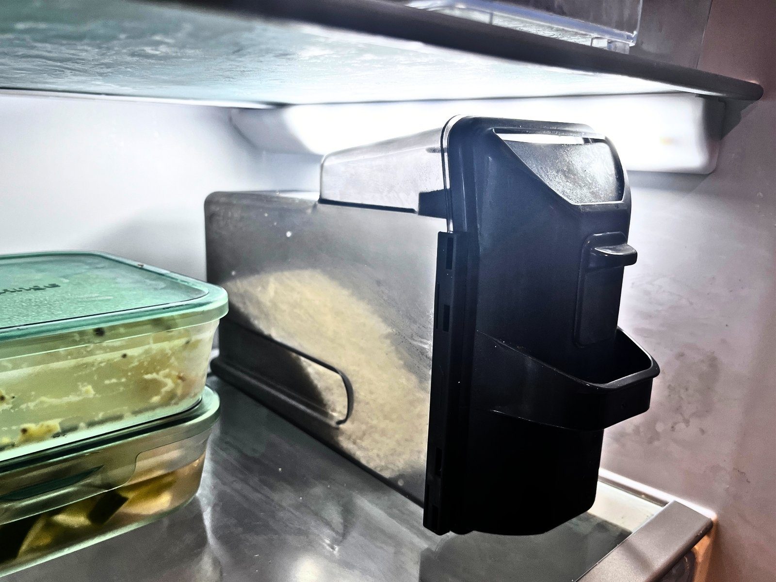 A slim black rice container with a measuring lever, kept on a fridge shelf