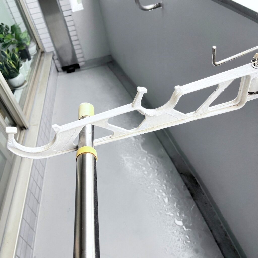 A drying pole passing through the outermost hole of a white wall bracket on a balcony