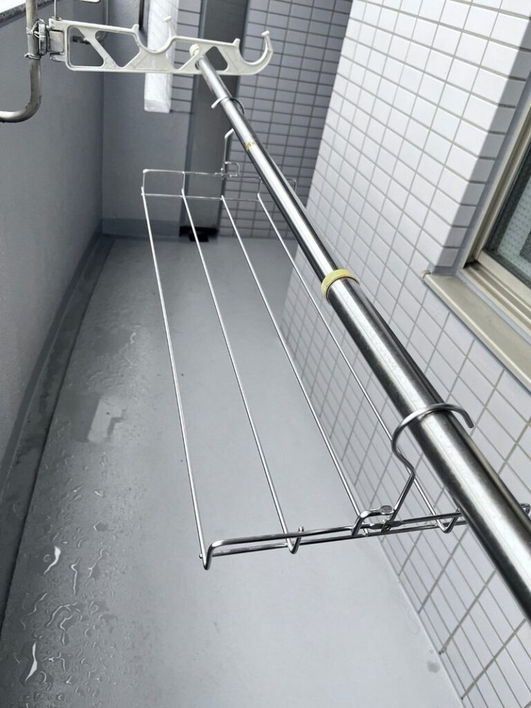 An empty flat stainless towel rack hooked onto a telescoping drying pole on a balcony