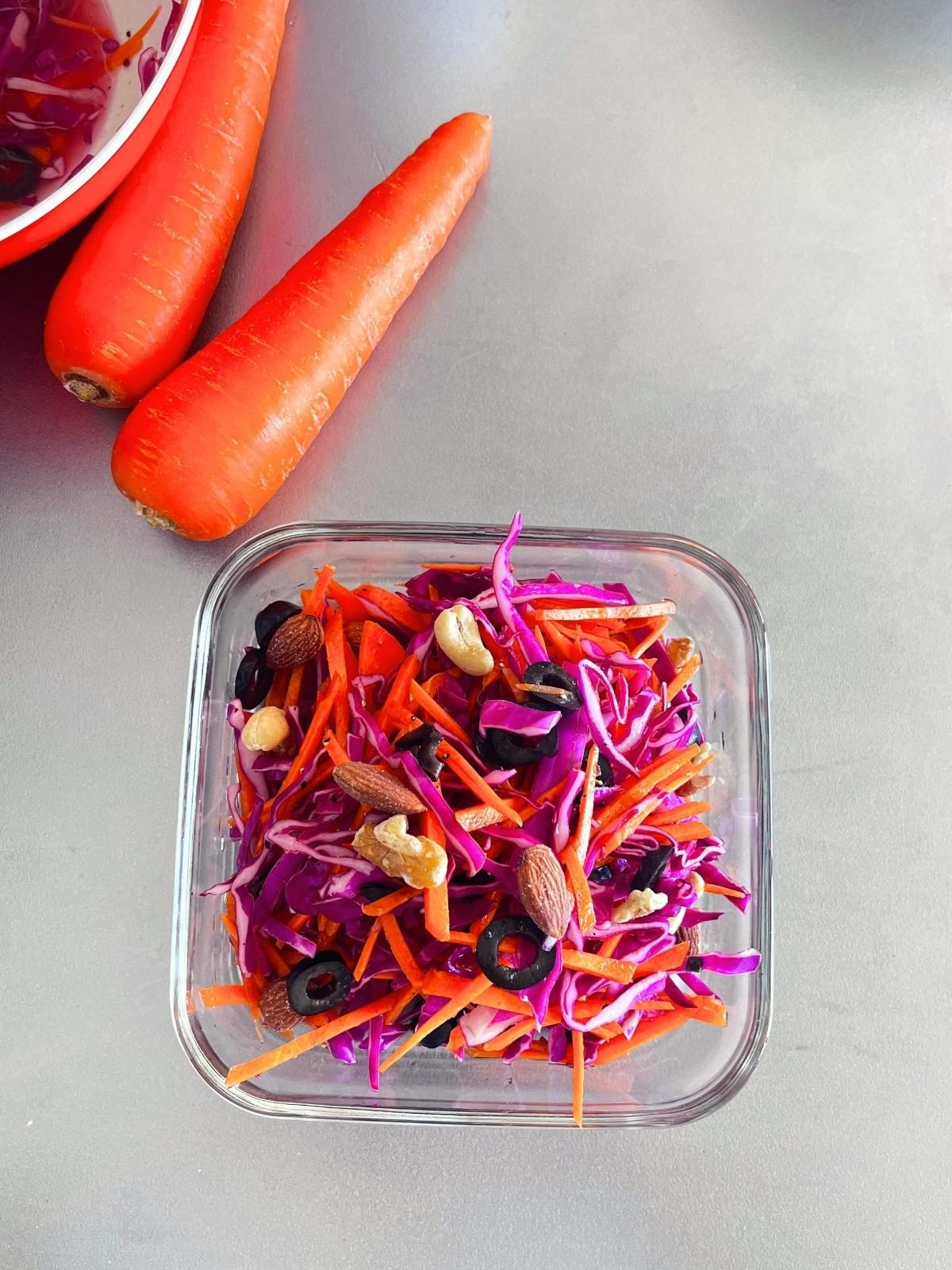 Red cabbage and carrot salad with nuts and olives in a square iwaki glass container