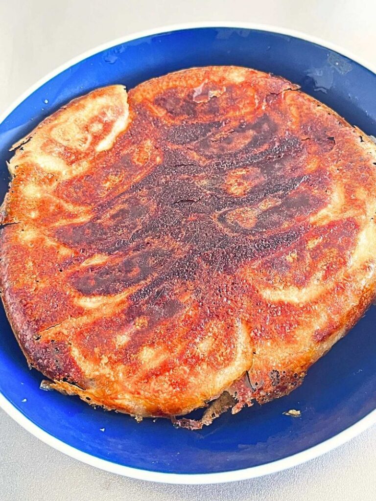 Pan-fried gyoza flipped onto a blue plate, crispy side up, joined by one golden wing
