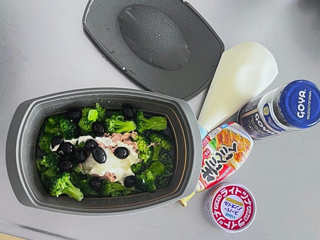 Steamed broccoli in a silicone steamer topped with tuna, black olives and mayo, with the ingredients beside it