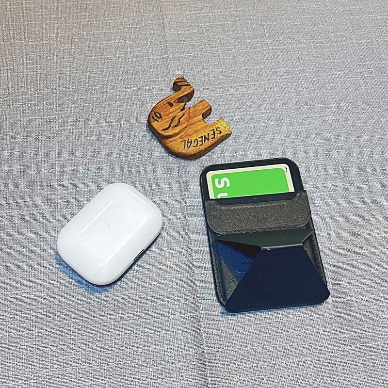 An AirPods case, a MagSafe card wallet and a wooden elephant fridge magnet on a gray cloth