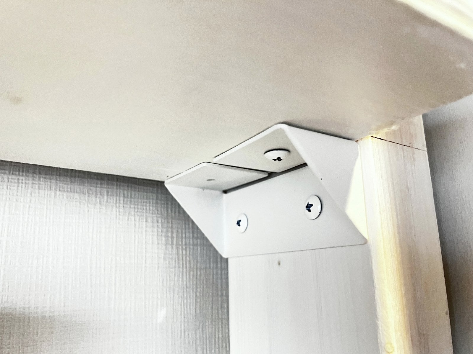 A white metal shelf bracket screwed to the side of a 2x4 post, under the shelf board