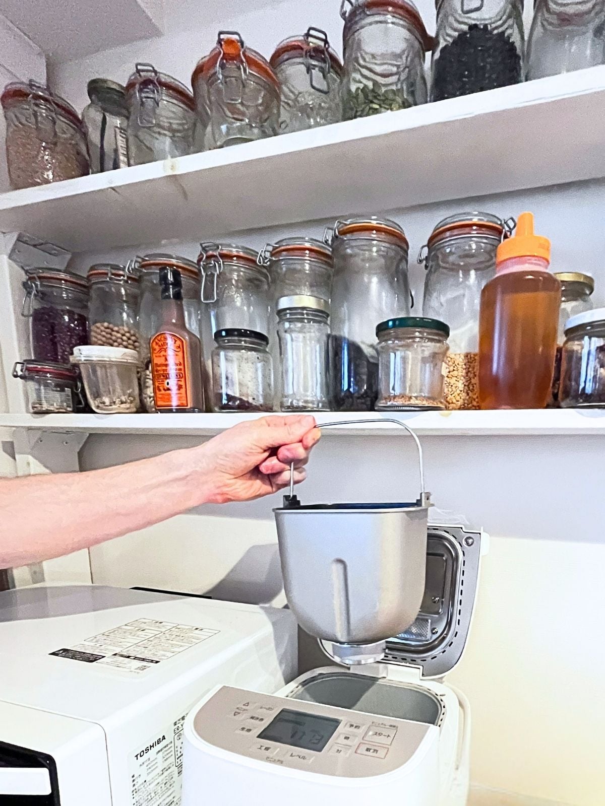 Two shelves seen from below, each holding a single row of glass jars