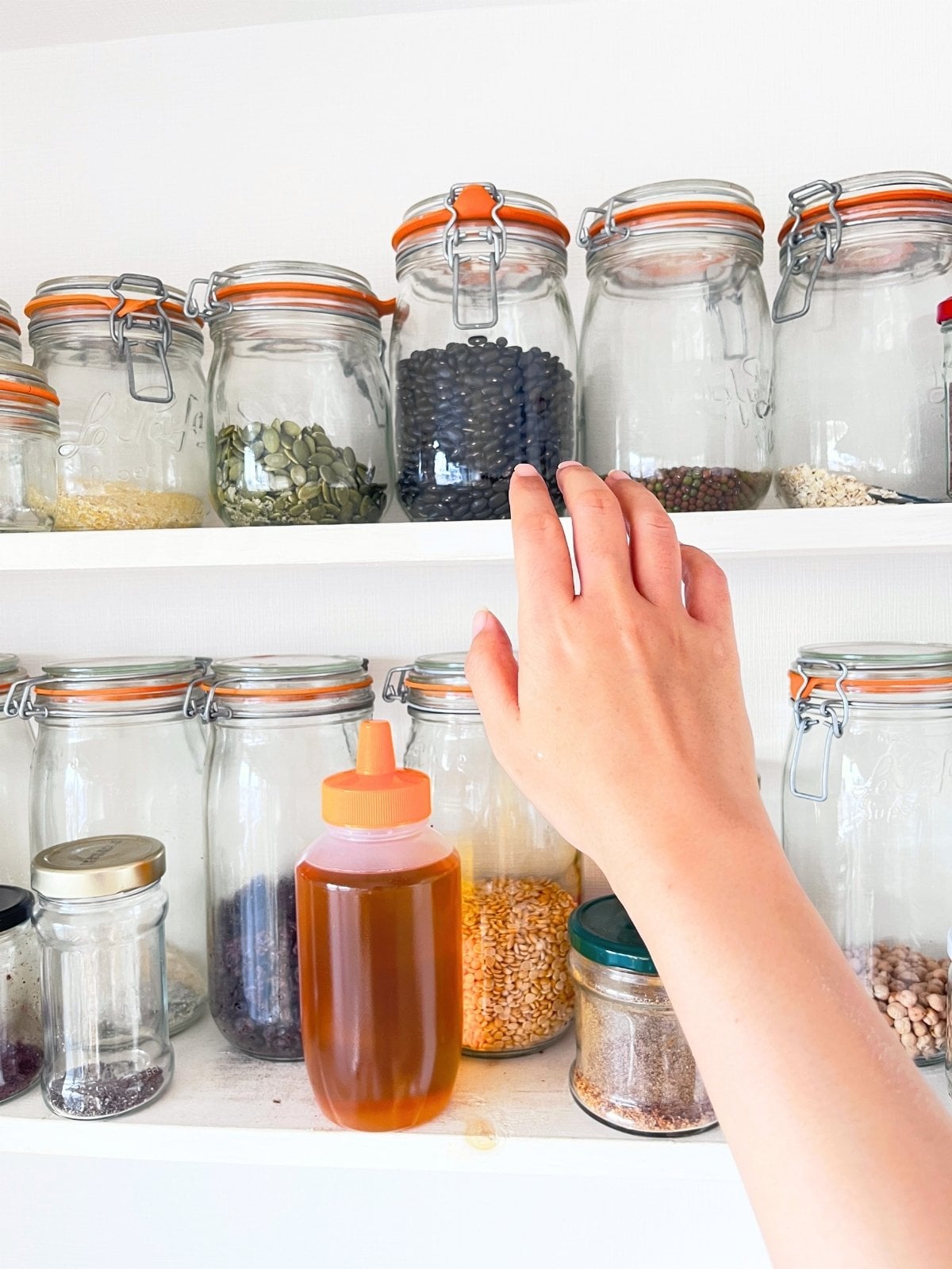 A hand reaching for a glass jar on the upper shelf