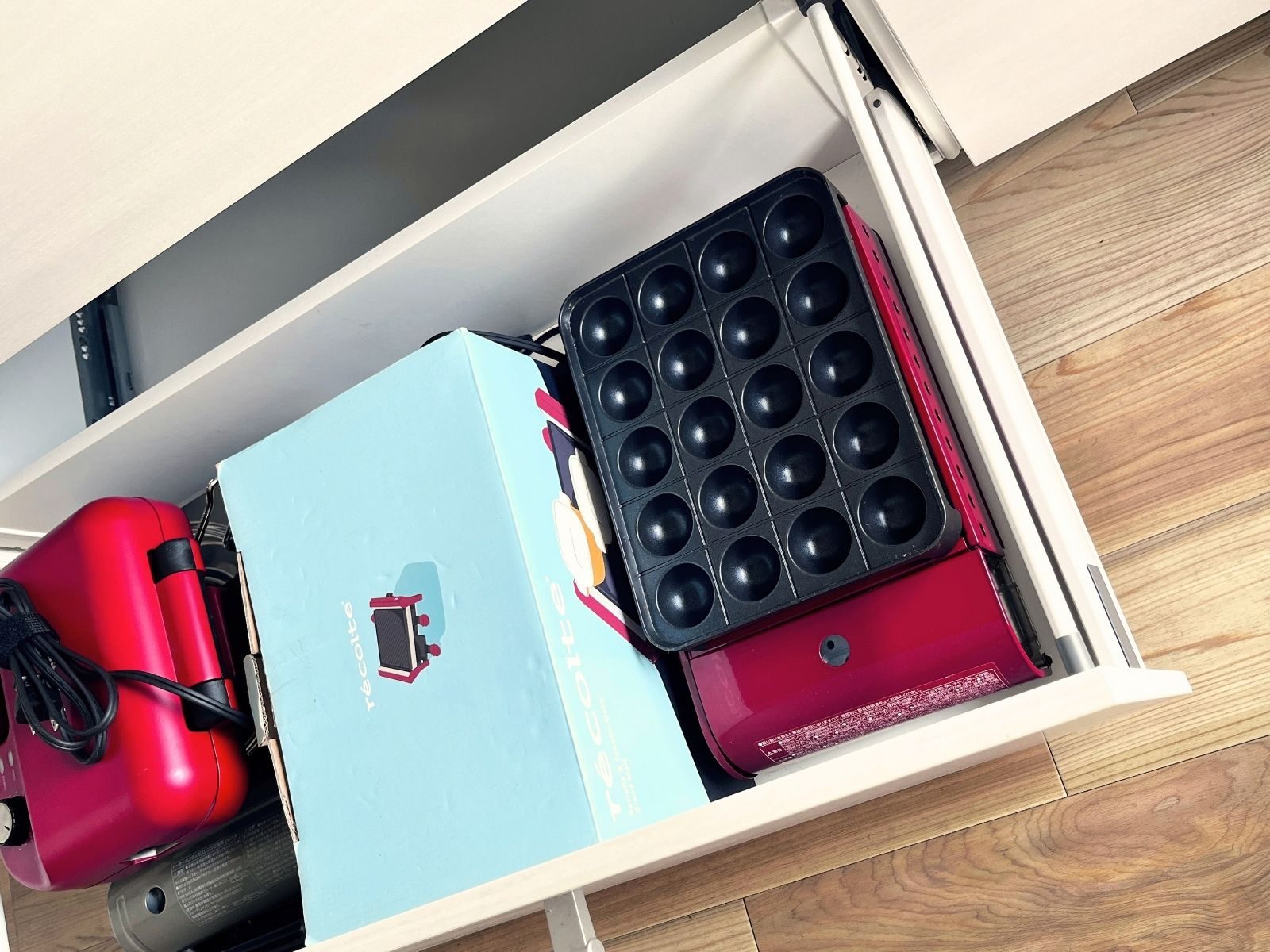 A takoyaki maker stored in a kitchen drawer with other tabletop cooking appliances