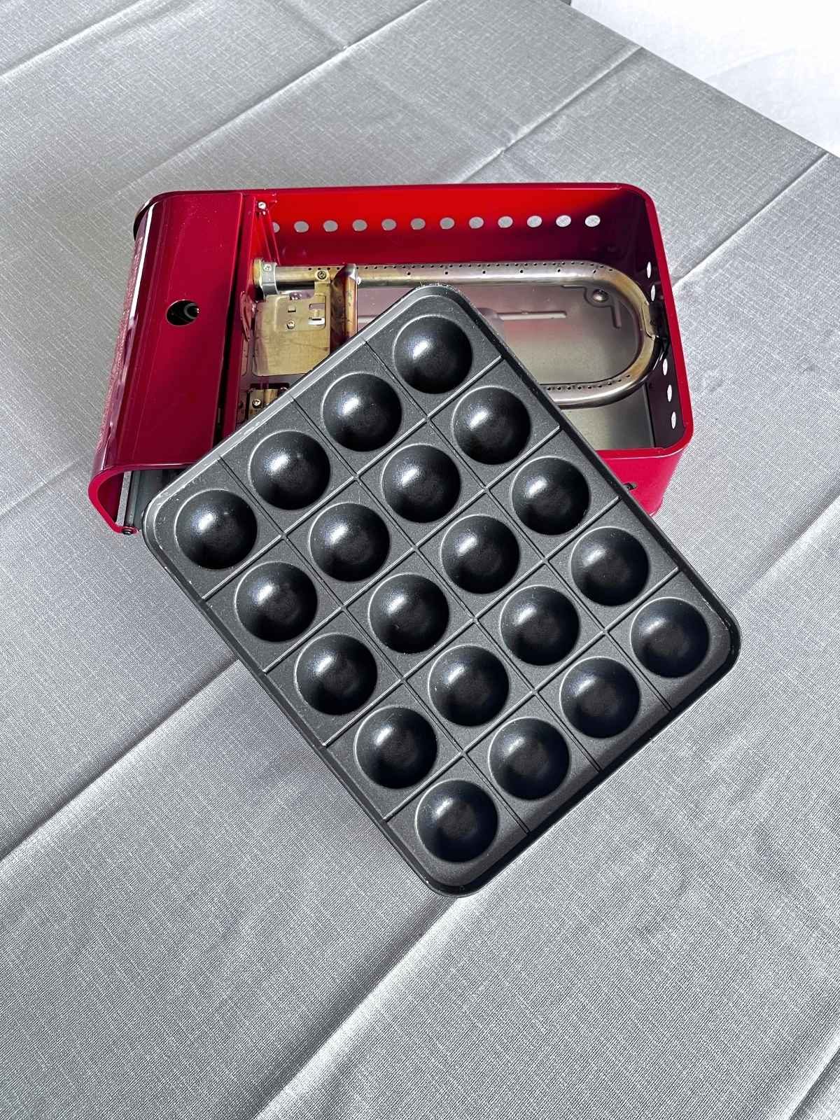 The cooking plate lifted out of a red butane takoyaki maker, showing the burner inside