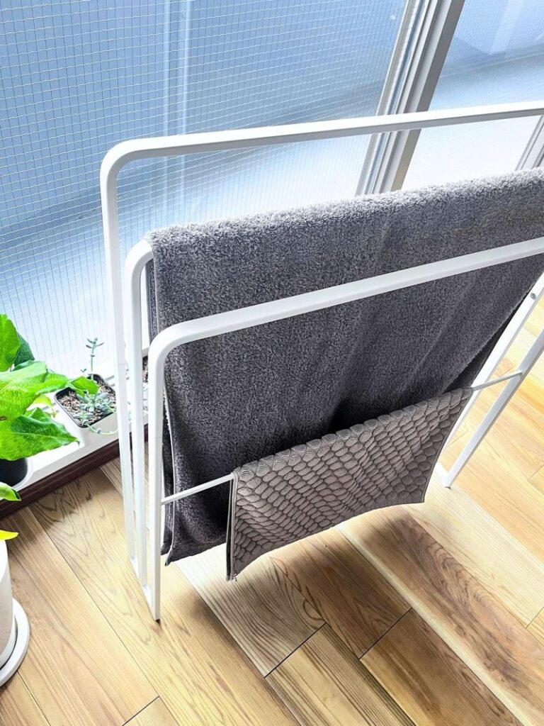 A gray bath towel and a bath mat hanging on the same stand, with the mat on the low bar underneath
