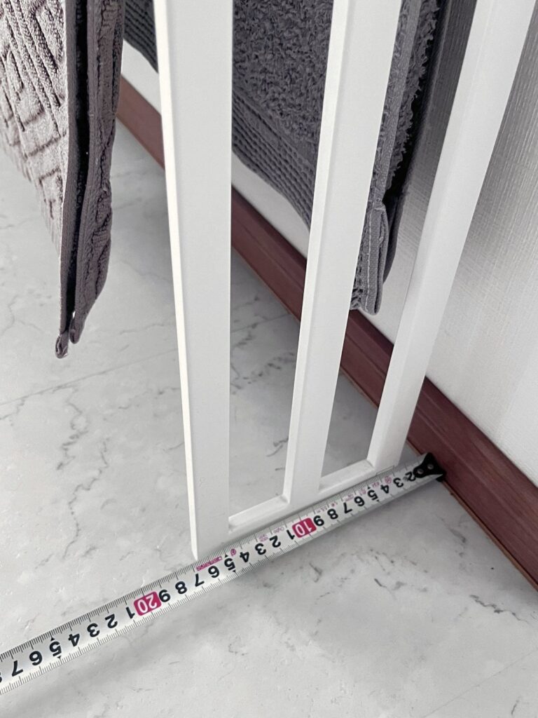 A tape measure at the foot of a white towel stand against the wall, showing how much floor depth the stand takes up