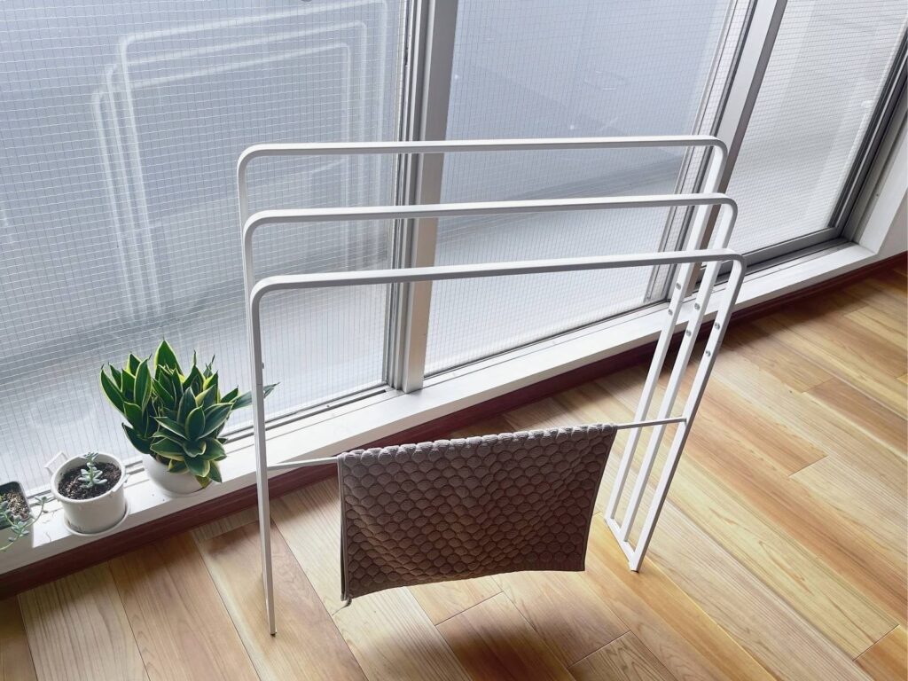 A bath mat hanging on the low mat bar of the towel stand