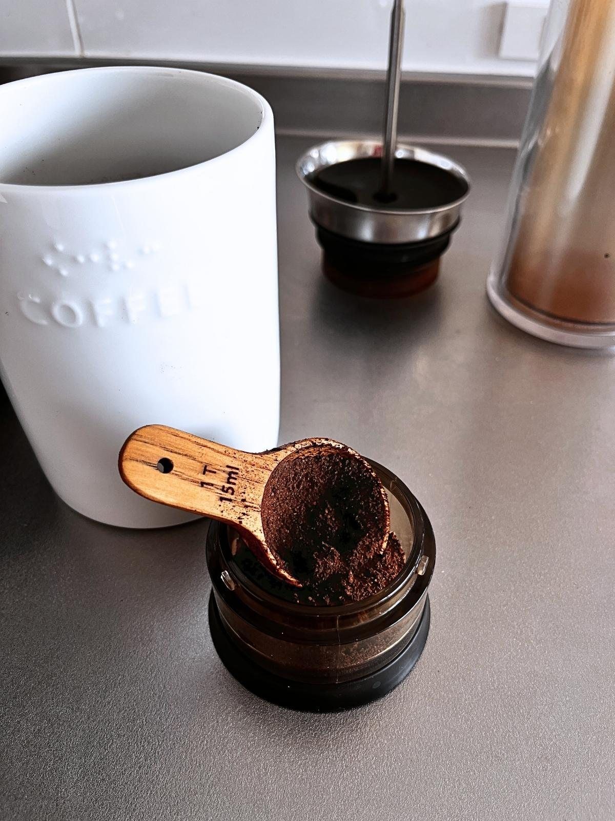 Spooning ground coffee into the American Press pod with a tablespoon measure