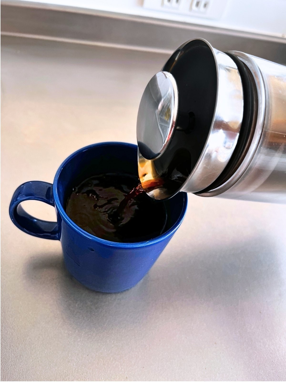 Pouring coffee from the American Press into a navy mug, up close
