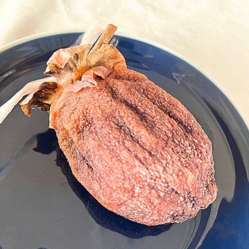 A homemade dried persimmon with its stem and a bit of plastic string, on a navy plate
