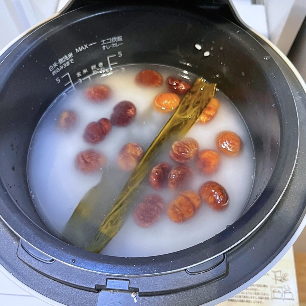 Roasted peeled chestnuts on top of rice and water in a rice cooker pot, with a piece of kombu, before cooking