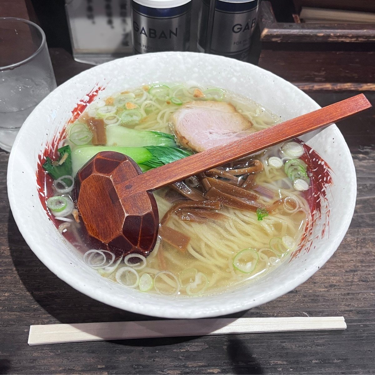 A bowl of shio ramen with a wooden spoon resting on top, on a wooden counter