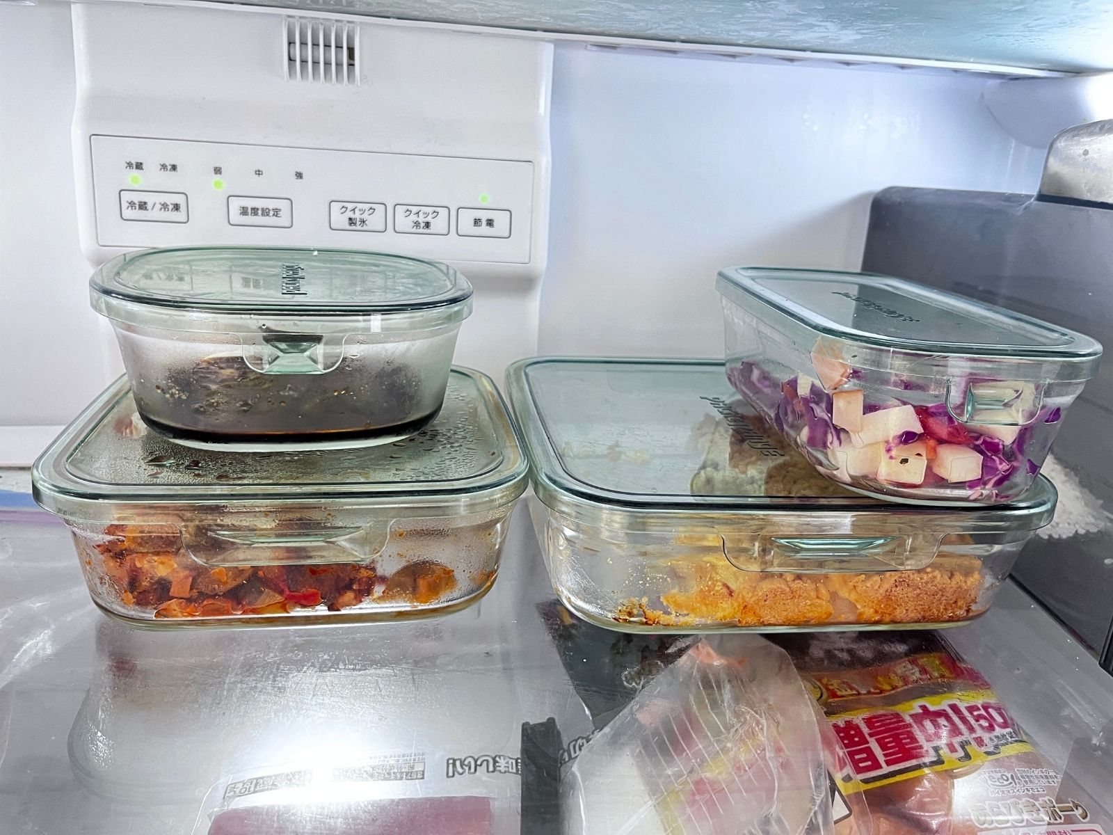 Four iwaki glass containers holding leftovers, stacked on a fridge shelf