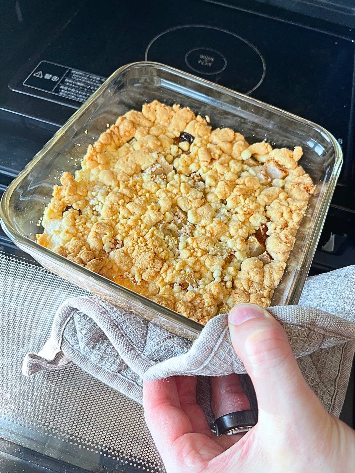 A fruit crumble just out of the oven, baked in a square iwaki glass container and held with a kitchen cloth