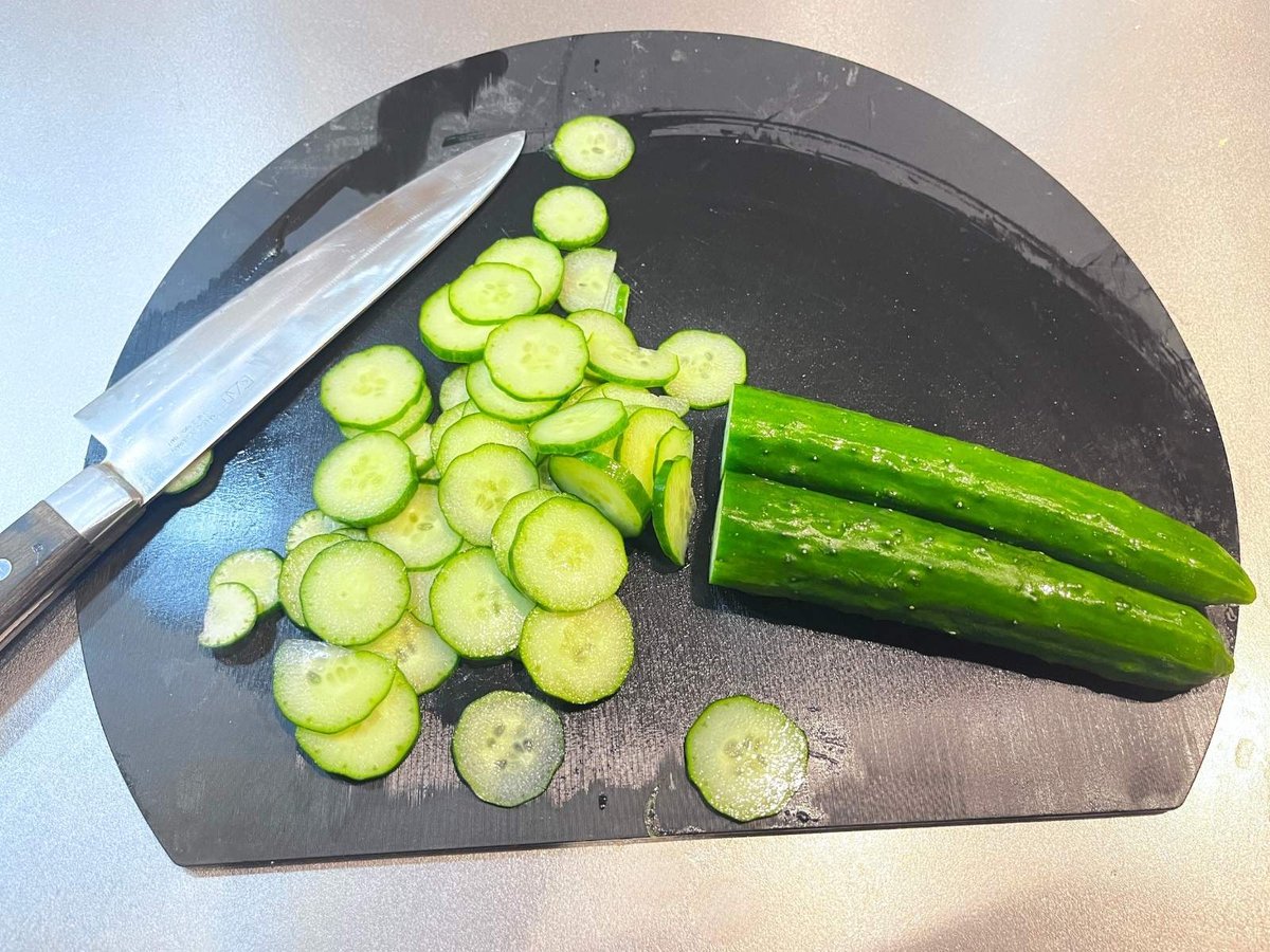 A cucumber sliced into thin rounds on a black cutting board, with a knife beside it