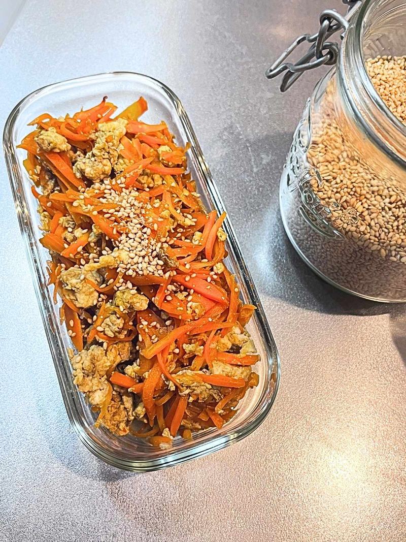 Carrot shirishiri with sesame seeds in a long glass container, with a jar of sesame seeds beside it