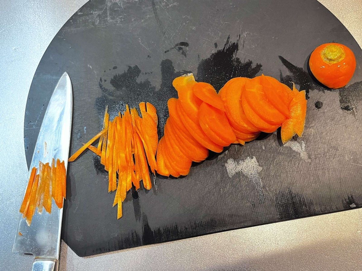 Carrot sliced into rounds and cut into thin strips on a black cutting board, with strips resting on the knife