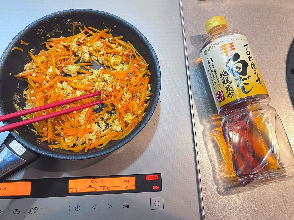 Carrot and egg stir-fried in a black pan, with a bottle of Mizkan shiro dashi on the counter beside it