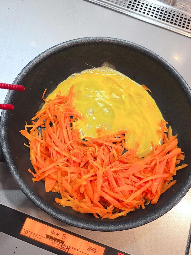 Beaten egg poured into the top half of the frying pan, with carrot strips in the bottom half
