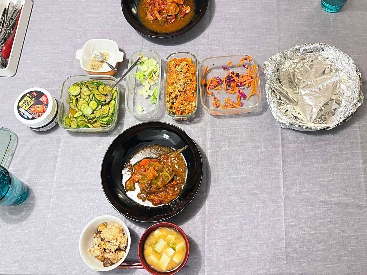 Dinner table seen from above: carrot shirishiri and sesame miso cucumber in glass containers, miso soup, chestnut rice and cabbage rolls in a black bowl