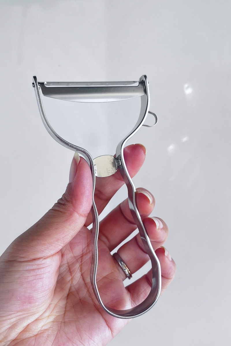 My left hand holding the Kai Select 100 peeler, fingers resting in the wavy handle