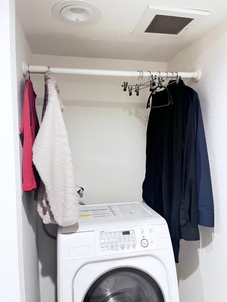 A tension rod above a front-loading washer, with clothes on hangers