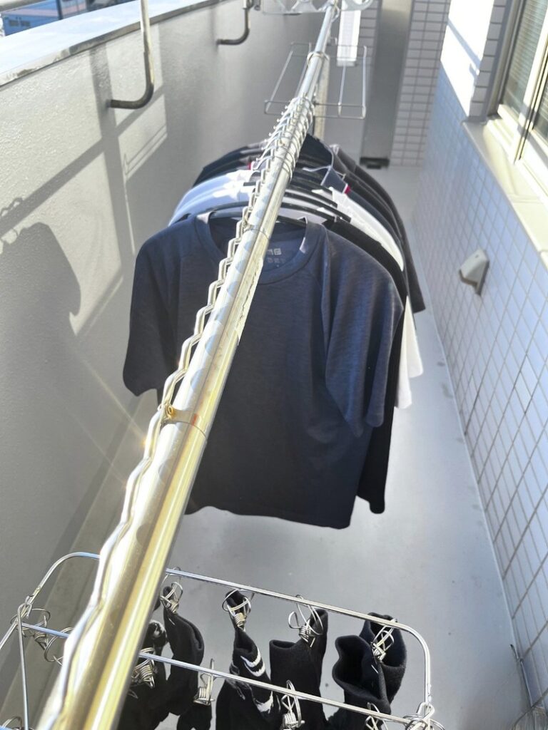 Laundry on hangers along a stainless drying pole on a balcony, with a towel rack at the far end and a pinch hanger of socks in front