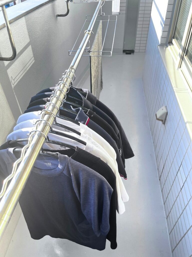 T-shirts on hangers along a telescoping drying pole, with a flat stainless towel rack hooked on further along