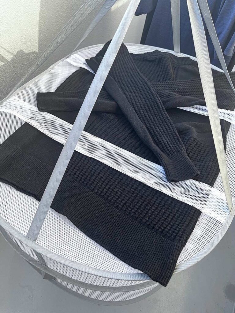 A black knit sweater laid flat on a hanging mesh drying rack
