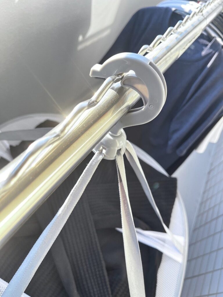 The swivel hook of a mesh drying rack hooked over a drying pole