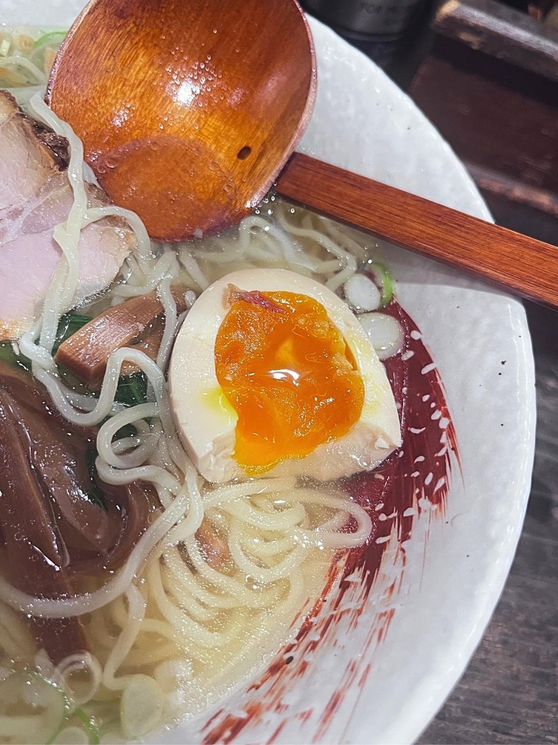 Half a marinated soft-boiled egg in shio ramen, next to a wooden spoon