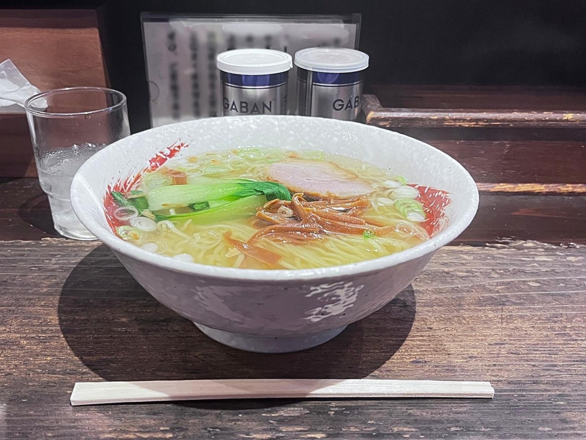 A bowl of shio ramen on a wooden counter, with chopsticks in front