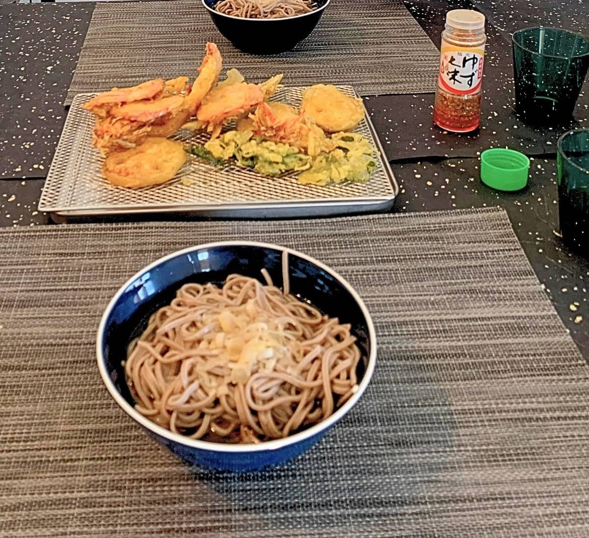 Toshikoshi soba in a navy bowl, with tempura of lotus root, sweet potato, fish, ham and shiso, and kakiage, on a tray behind it