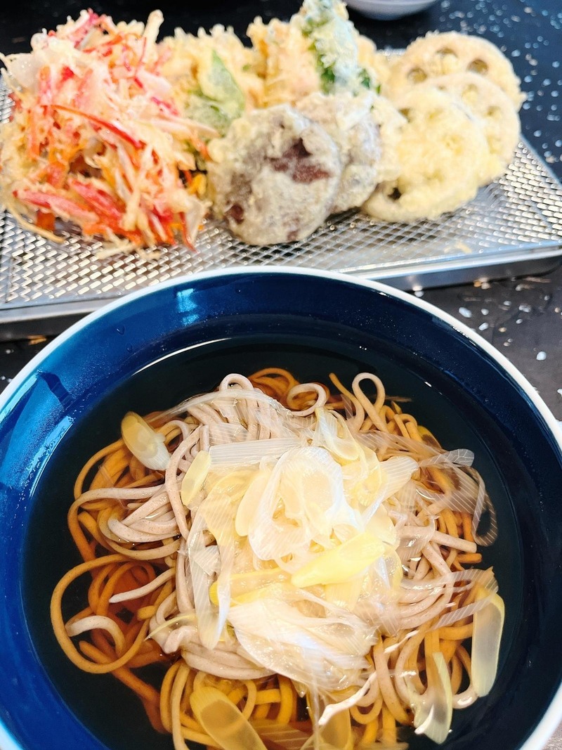 Toshikoshi soba in a navy bowl with lots of sliced Japanese long green onion, and a tray of tempura behind it