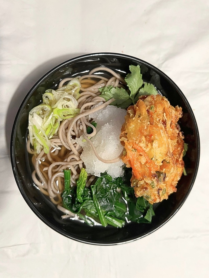 Toshikoshi soba in a black bowl with kakiage, grated daikon, spinach, mitsuba and Japanese long green onion