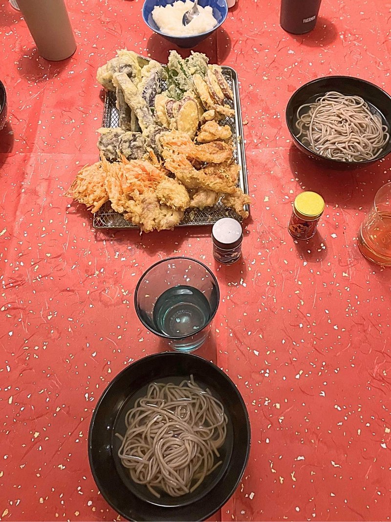Two bowls of soba and a big plate of tempura on a red tablecloth