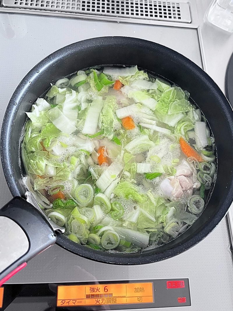 A 20 cm pan with the detachable handle attached, simmering napa cabbage, carrot, green onion and chicken drumettes in clear broth