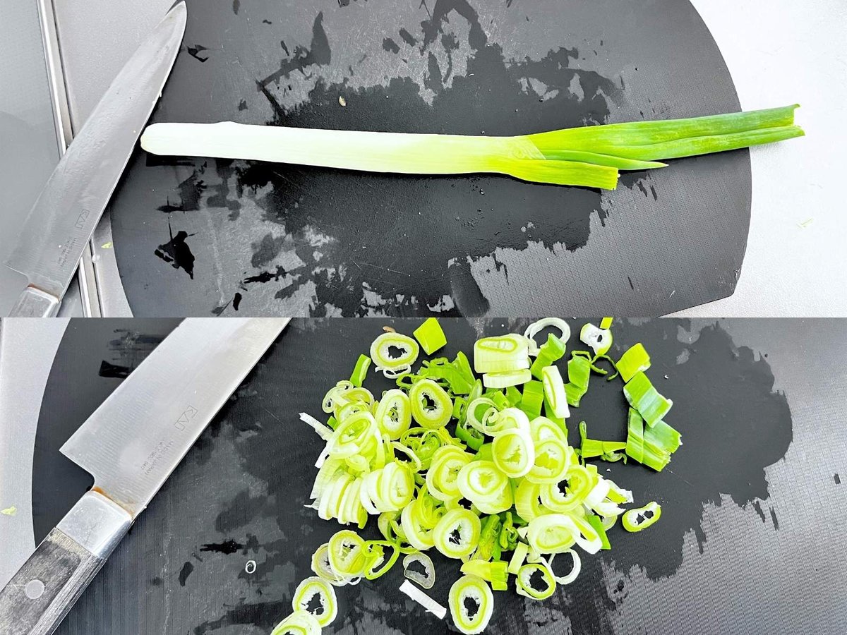 A whole green onion above sliced green onion on a black cutting board, with a knife