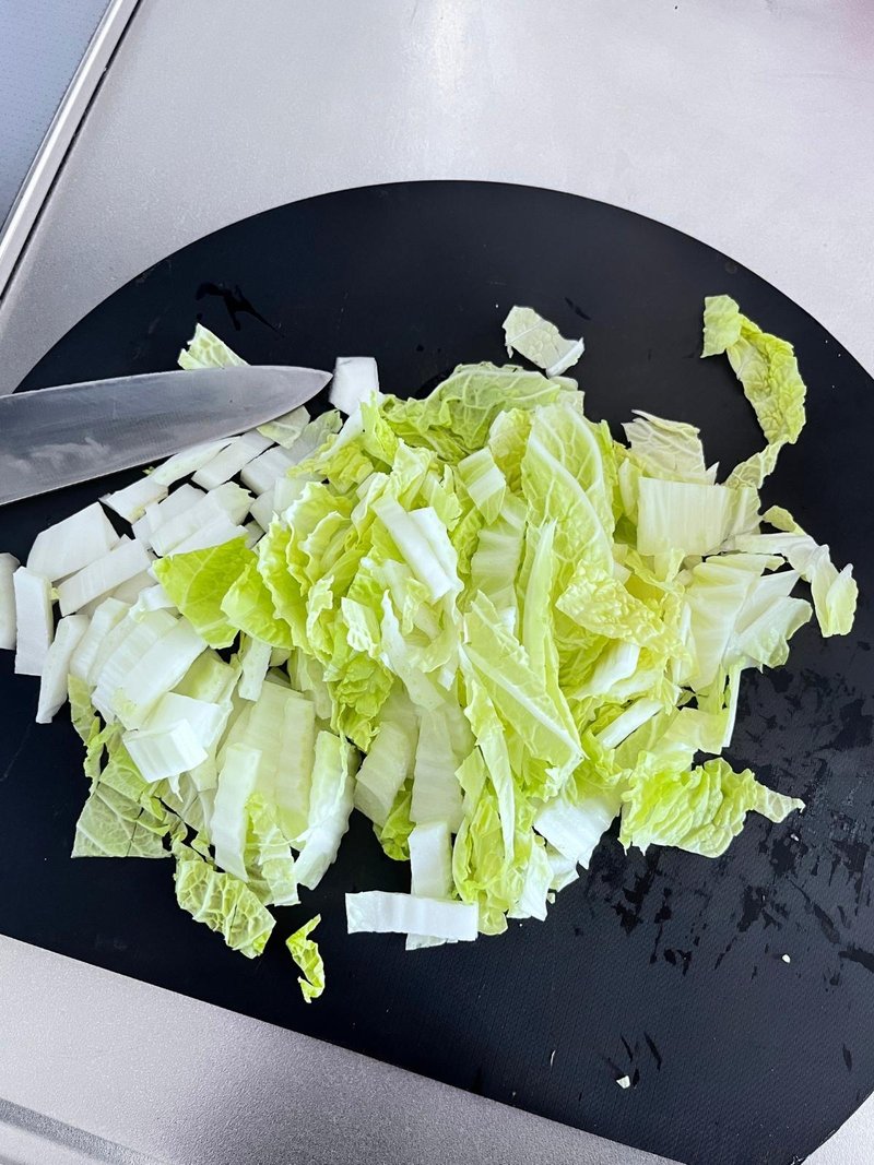 Napa cabbage cut into pieces on a black cutting board, with a knife